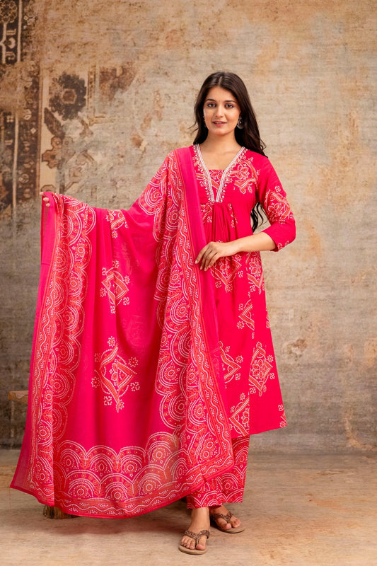 Woman wearing a bright pink traditional outfit with white patterns against a textured wall.